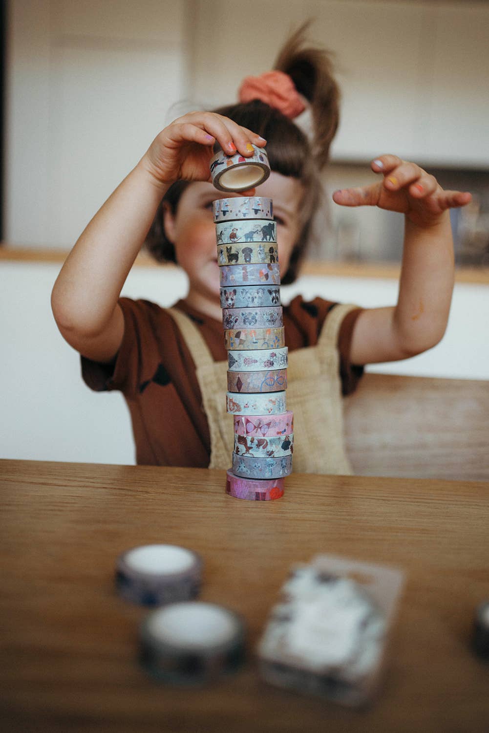 Child playing with a stack of colorful tape rolls on a wooden table.