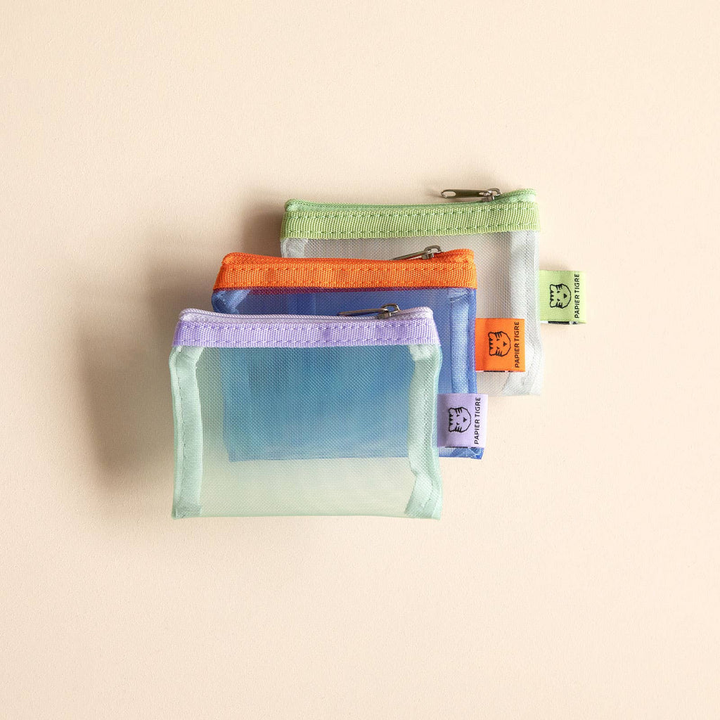 Set of three transparent mesh pouches with colorful zippers on a beige background