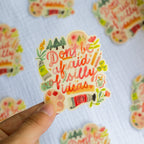 Colorful sticker with 'Don't be afraid of silly ideas' text held by a hand on a patterned background.
