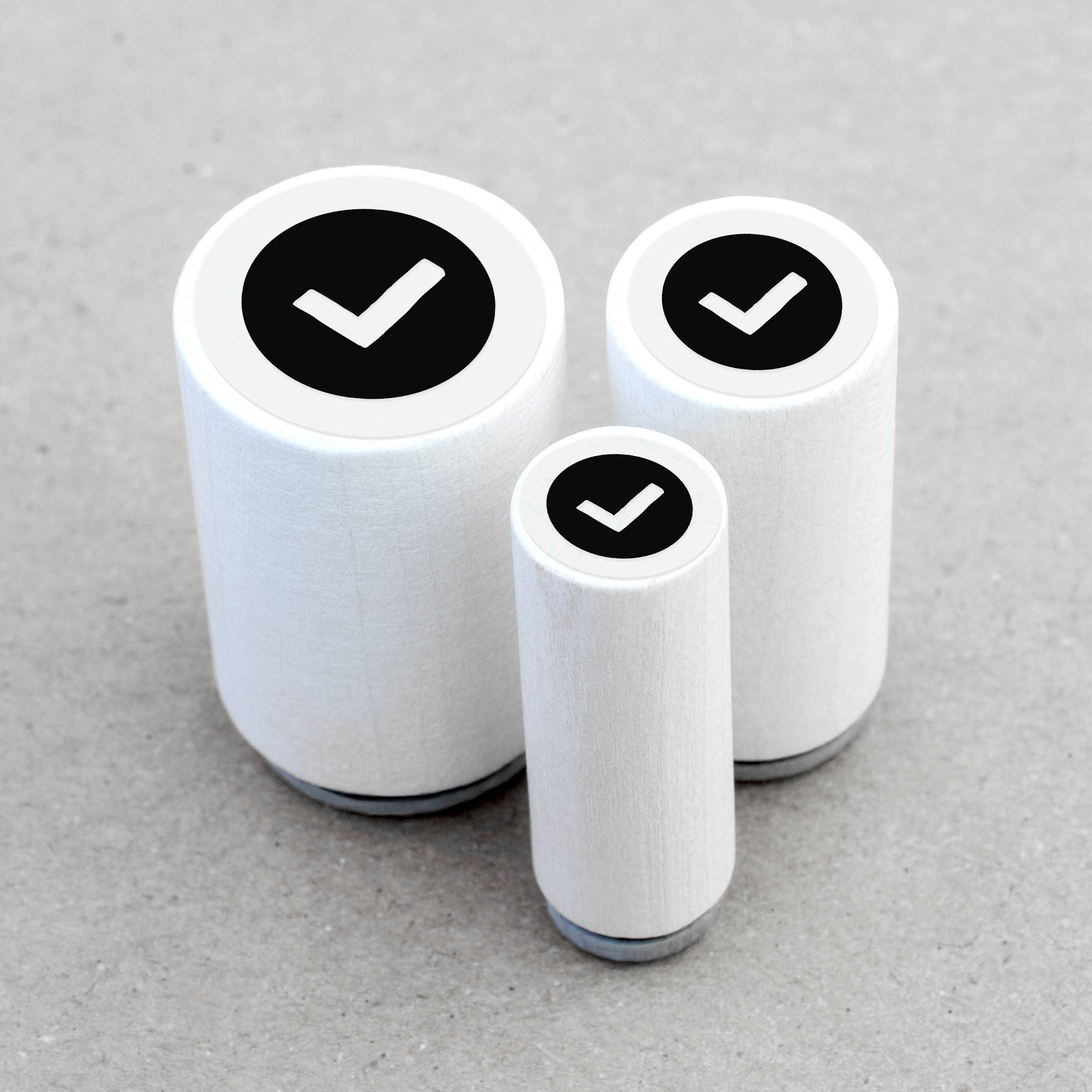 Three cylindrical white stamps with black check marks on a gray background