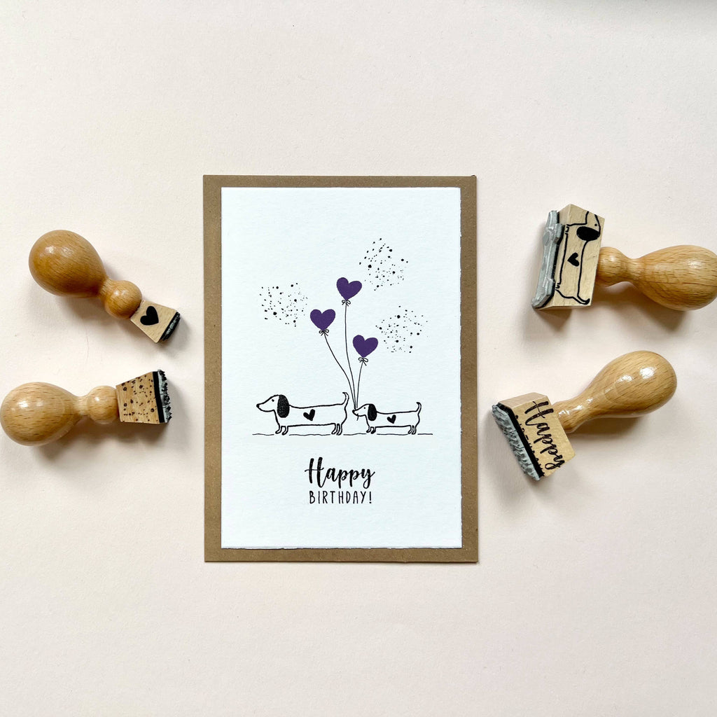 Framed birthday card with dachshunds and hearts, surrounded by wooden stamps on a light background