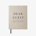 A linen-textured hardcover notebook with black printed text reading 'DEAR GUEST' and 'Share a line or two' on a clean white background.