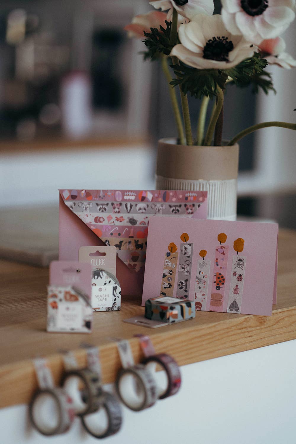 Decorative items including a vase with flowers, stationery, and washi tape on a wooden surface.