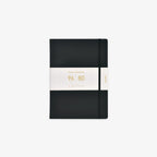 A black hardcover notebook with an elastic closure band and a white paper band around the middle, featuring gold text that reads 'Classic Notebook 96 sheets and 80gsm'.