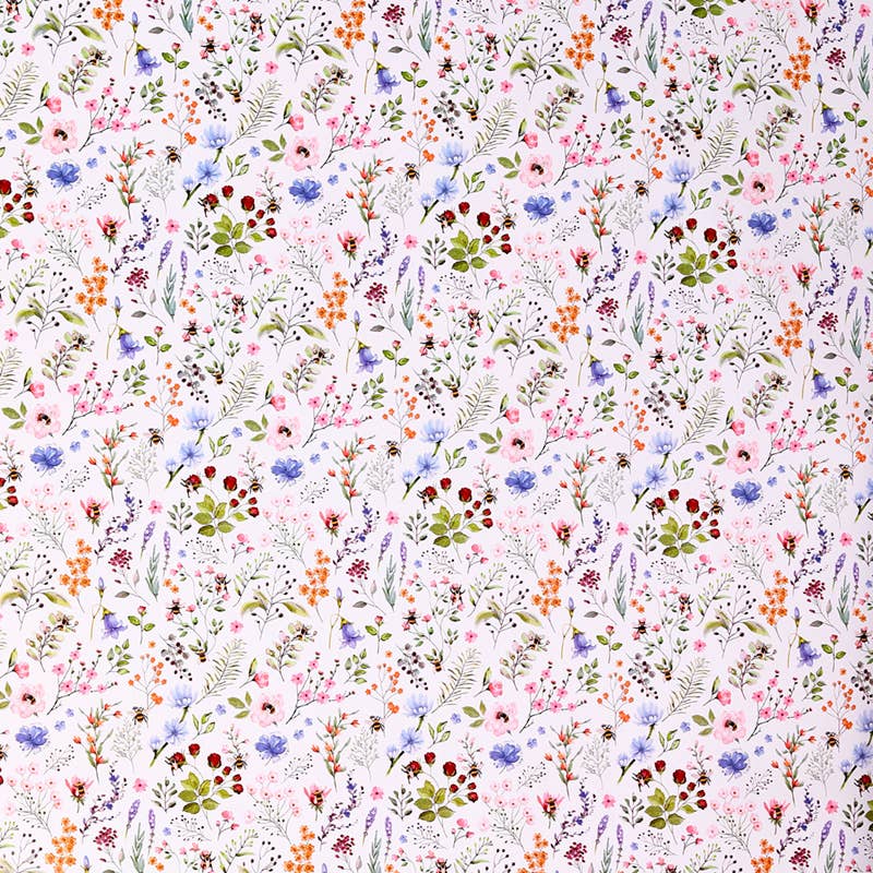 A close-up of a white fabric with a dense, all-over watercolor floral print featuring pink, blue, green, orange, and red wildflowers and leaves.