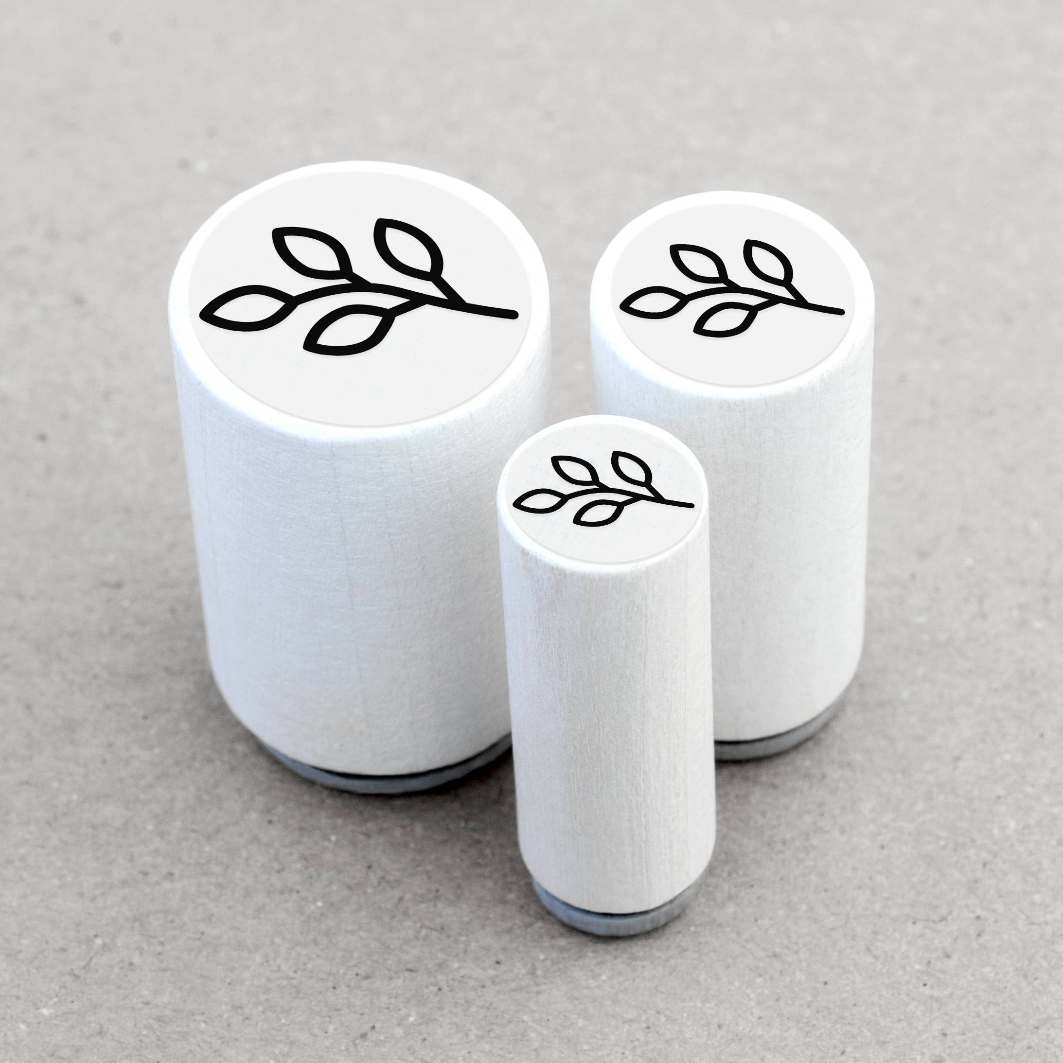 Three white cylindrical stamps with leaf designs on a gray background