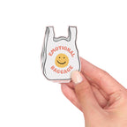 Vinyl sticker of Small white bag with 'Emotional Baggage' text and smiley face held by a hand on a white background