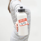 Person holding a white water bottle with a vinyl sticker 'Ask Me About My Dog' on a plain background