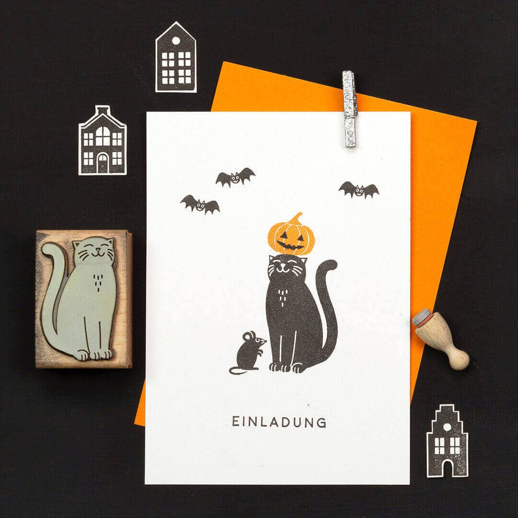 Halloween-themed card with a cat, pumpkin, and bats on a black background.