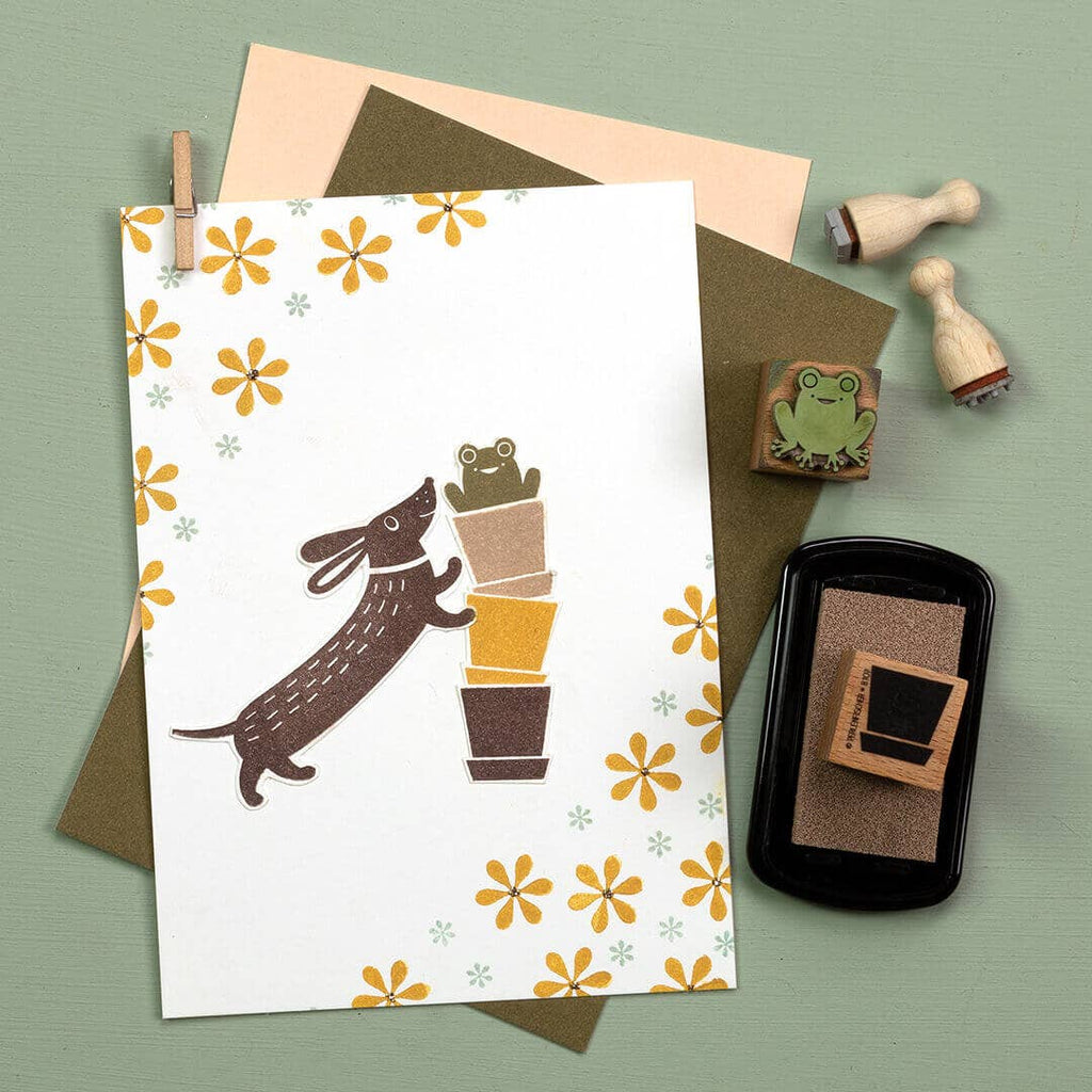 Greeting card with dog and potted plant illustration, envelope, and stamps on a green background