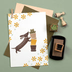 Greeting card with dog and potted plant illustration, envelope, and stamps on a green background