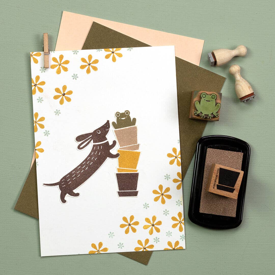 Greeting card with dog and potted plant illustration, envelope, and stamps on a green background