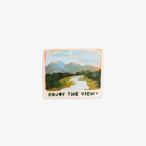 A rectangular sticker with rounded corners featuring a hand-drawn landscape illustration of mountains, a winding river, and green fields. The sticker has an orange border and the text 'ENJOY THE VIEW' printed at the bottom.