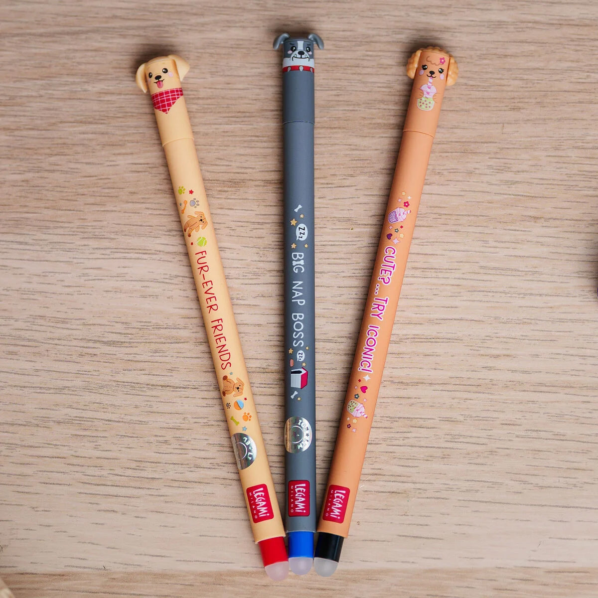 Three erasable gel pens with dog-themed designs on a wooden surface