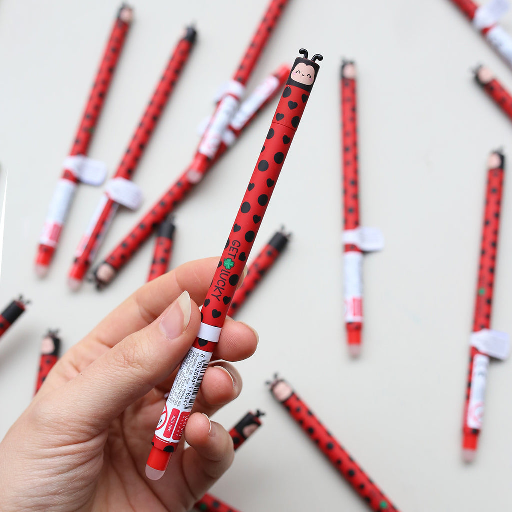 Hand holding a red and black ladybug-themed pen with more pens in the background.
