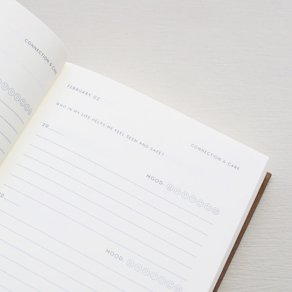 Open notebook with a page showing text prompts and emoji icons from 'Treårsdagbogen' on a light background
