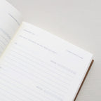 Open notebook with a page showing text prompts and emoji icons from 'Treårsdagbogen' on a light background