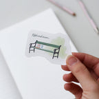 Hand holding a sticker with a Copenhagen bench design and 'København' text on a light background.
