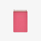 Pink notebook with gold spiral binding on a white background