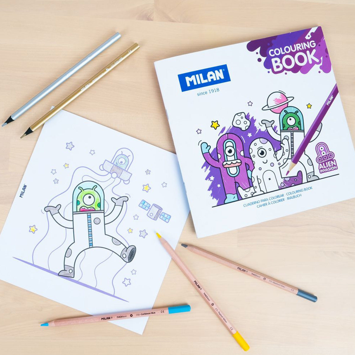 Coloring book with alien design and pencils on a wooden surface