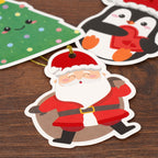 Cartoon Santa Claus gift tag on a wooden surface with other Christmas-themed stickers.