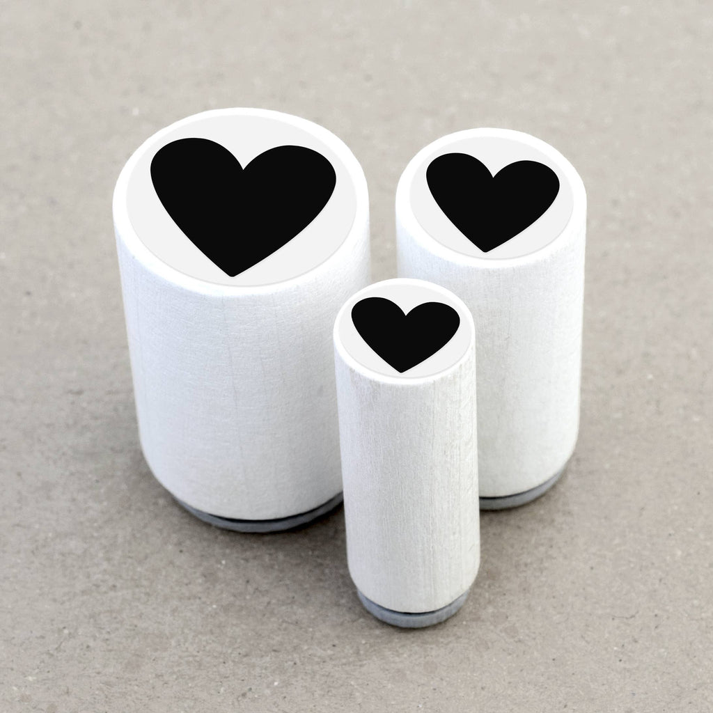 Three wooden rubber stamps with black heart shapes on a gray background