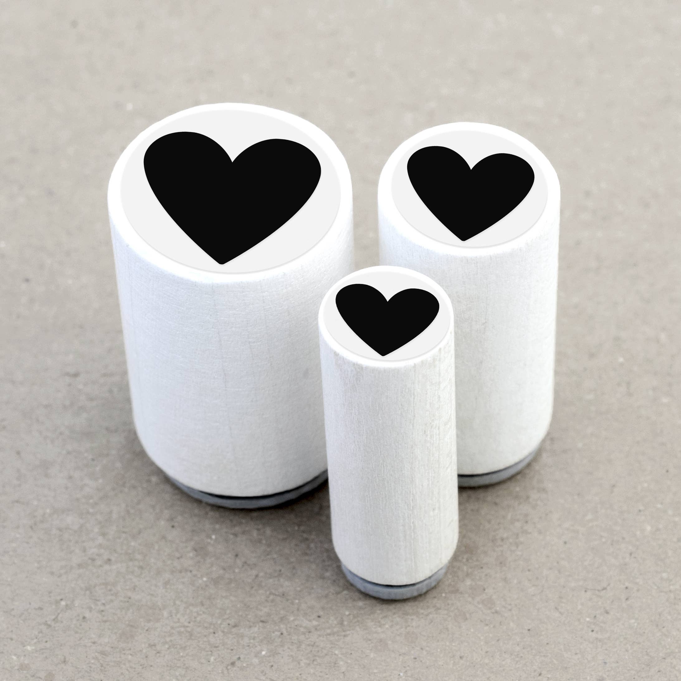 Three wooden rubber stamps with black heart shapes on a gray background