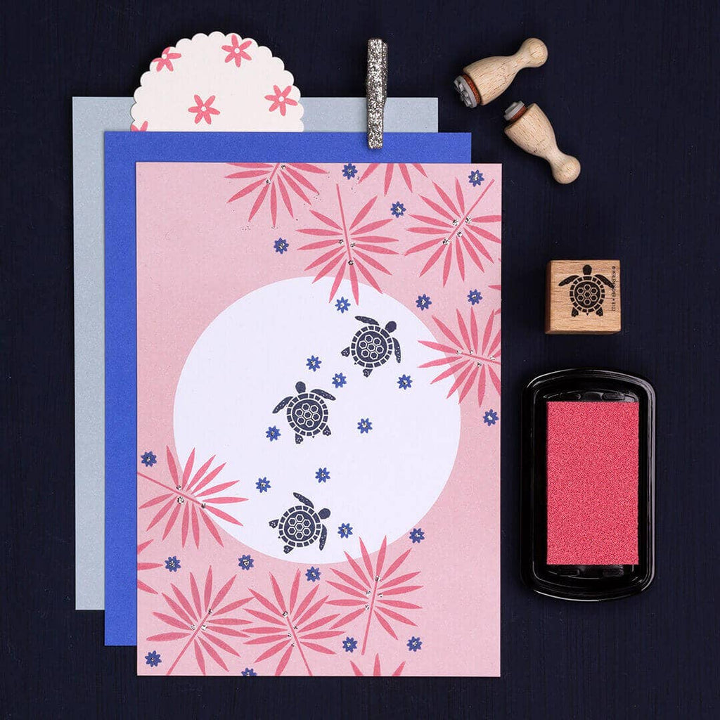 Card with turtle design and floral patterns, surrounded by stamps and ink pad on a dark background