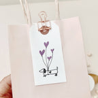Gift tag with a dog and heart balloons design on a pink bag.