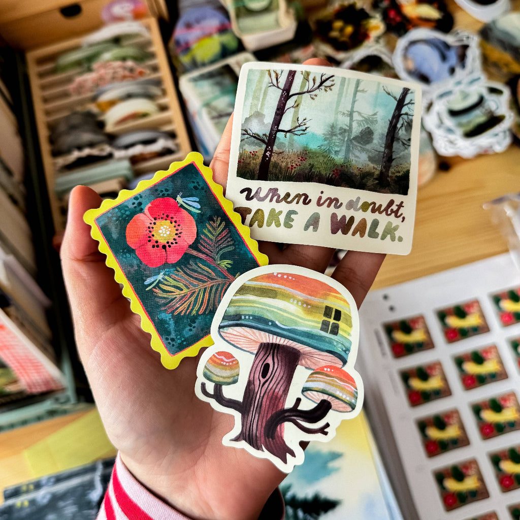 Hand holding colorful stickers with nature-themed designs and text.