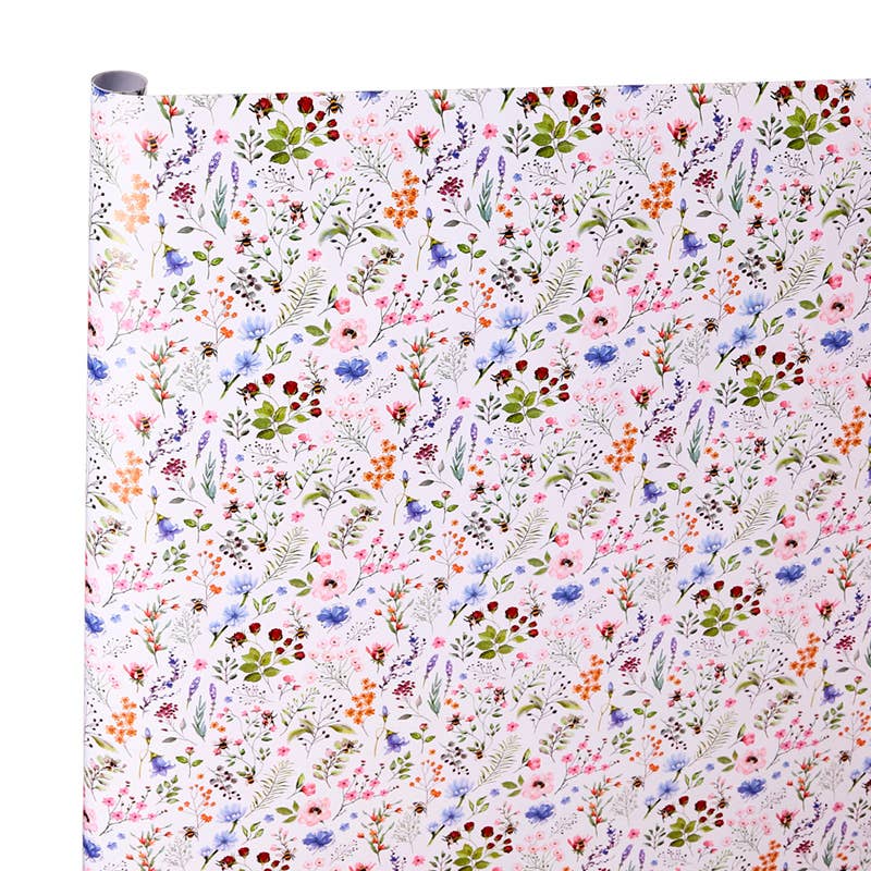 A roll of wrapping paper or fabric with a dense, multicolor floral and botanical pattern on a white background, shown against a plain white backdrop.