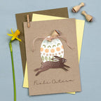 Greeting card with Easter design featuring a rabbit and egg, placed on a blue surface with a yellow flower and wooden stamps.